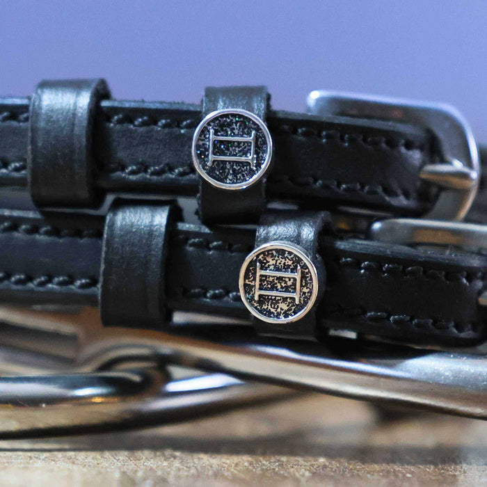 Close-up of round Gemini zodiac charms on black leather ManeJane spur straps