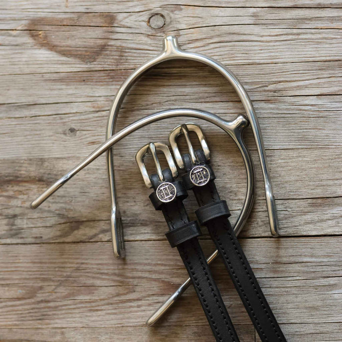 ManeJane Gemini spur straps with zodiac charms laid on wood beside a silver spur