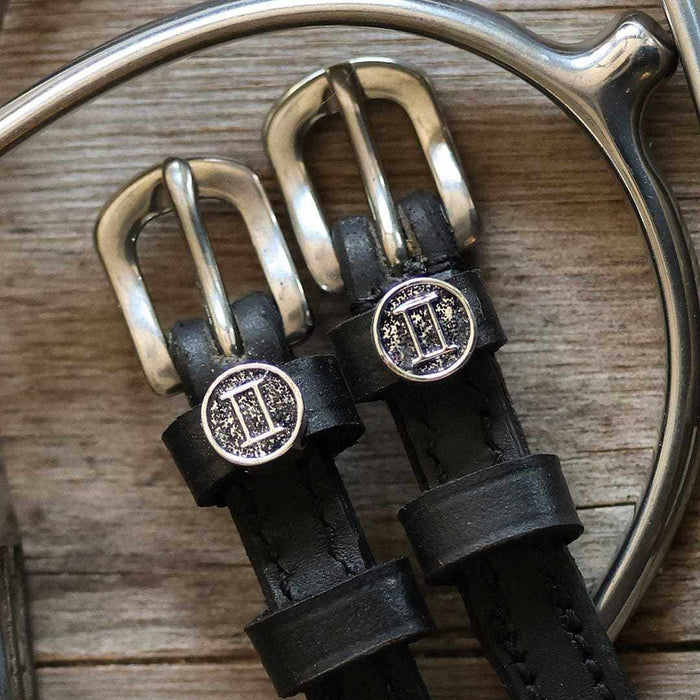Gemini zodiac charms on black spur straps resting on a silver stirrup, ManeJane detail