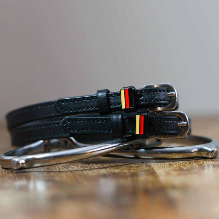 Black leather German flag spur straps coiled beside a silver spur on a wooden surface
