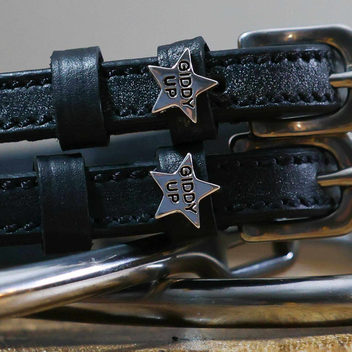 Close-up of silver 'Giddy Up' star charms on black leather spur strap keepers