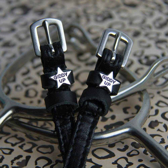 Close-up of black-enamel 'Giddy Up' star charms on spur straps over a leopard print