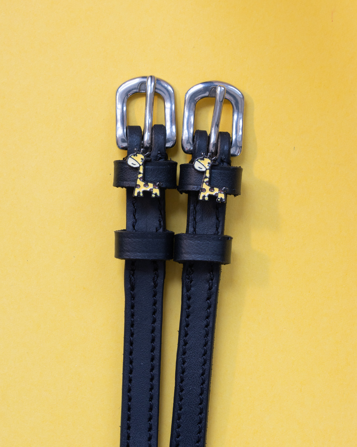 Black leather ManeJane Giraffe spur straps with silver buckles and giraffe charms on yellow