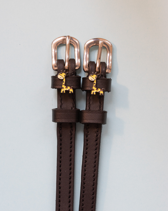 Dark brown Giraffe spur straps with rose gold buckles and giraffe charms on pale grey