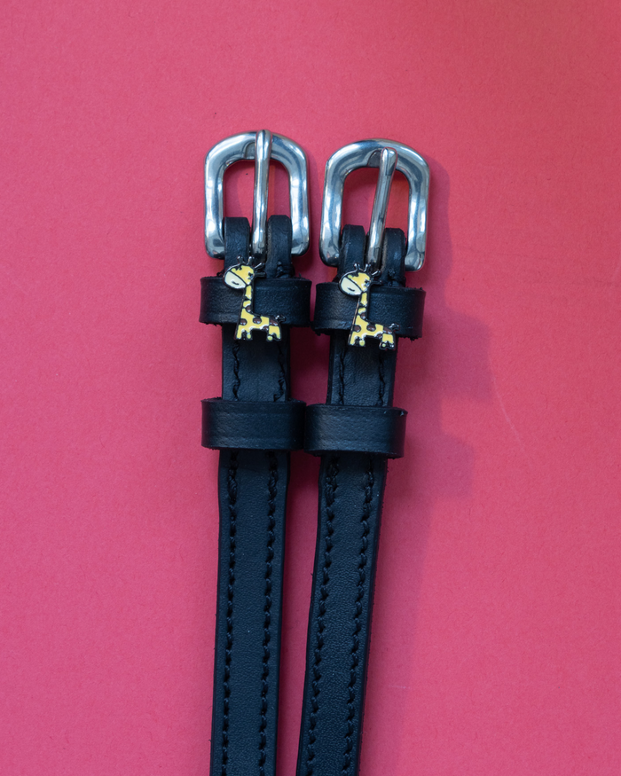 Black leather ManeJane Giraffe spur straps with silver buckles on a red background