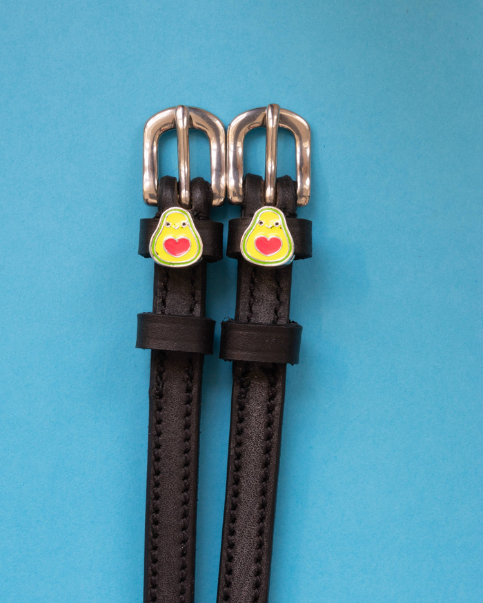 Happy avocado spur straps in black leather laid flat on a blue background