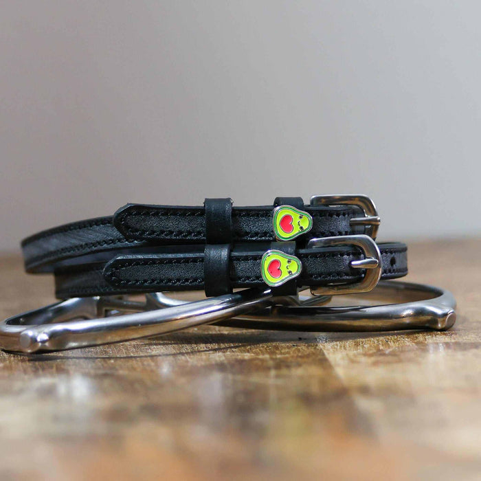 Coiled black leather spur straps and a silver spur on wood with avocado heart charms