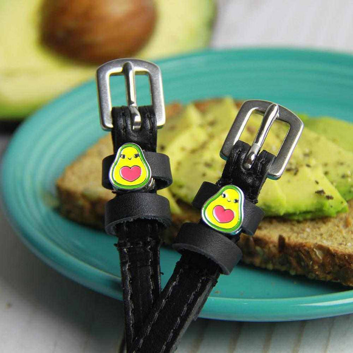Avocado-charm ManeJane spur straps resting on avocado toast on a teal plate