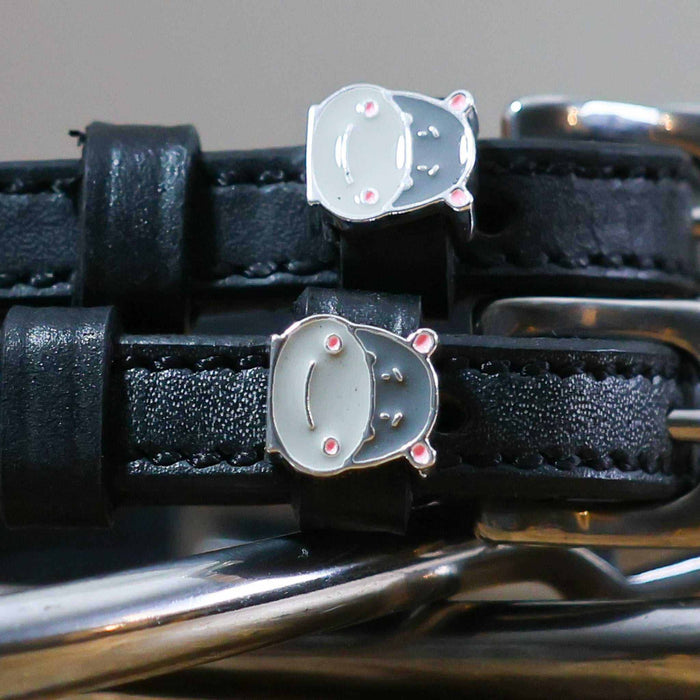 Close-up of grey hippo face charms on black leather spur straps over spur hardware