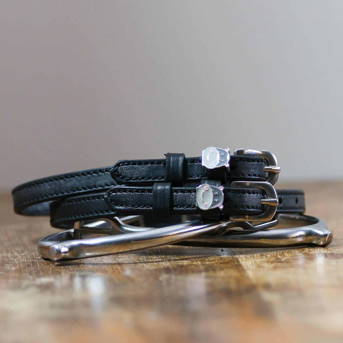 ManeJane Hippo Face spur straps coiled beside silver spurs on a wooden table