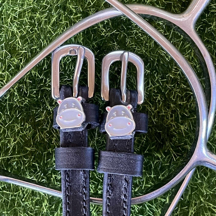 Black leather Hippo Face spur straps with silver hippo charms on grass beside a spur
