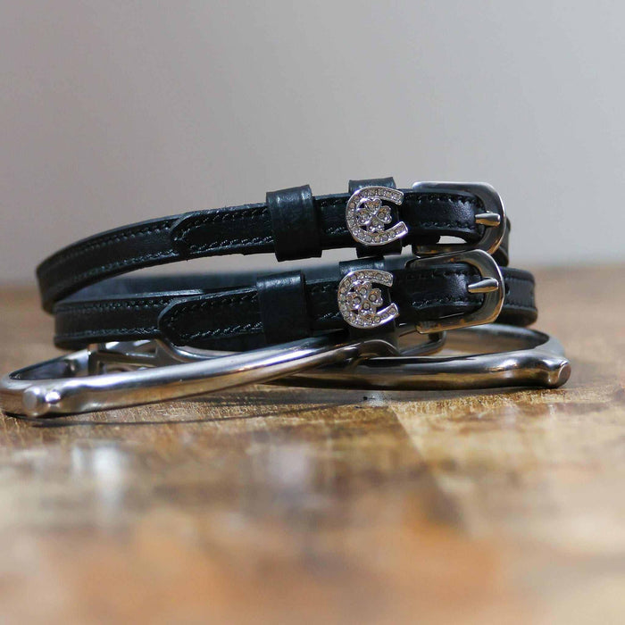 Coiled black leather spur straps with sparkling horseshoe-clover charms stacked on a spur