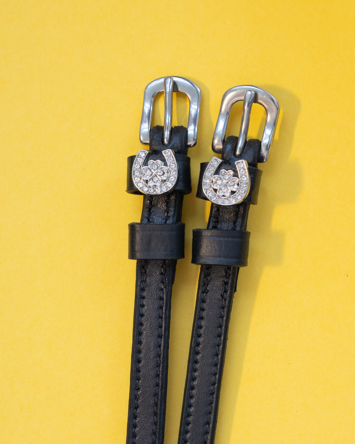 Black leather horseshoe clover spur straps with crystal charms on a yellow background