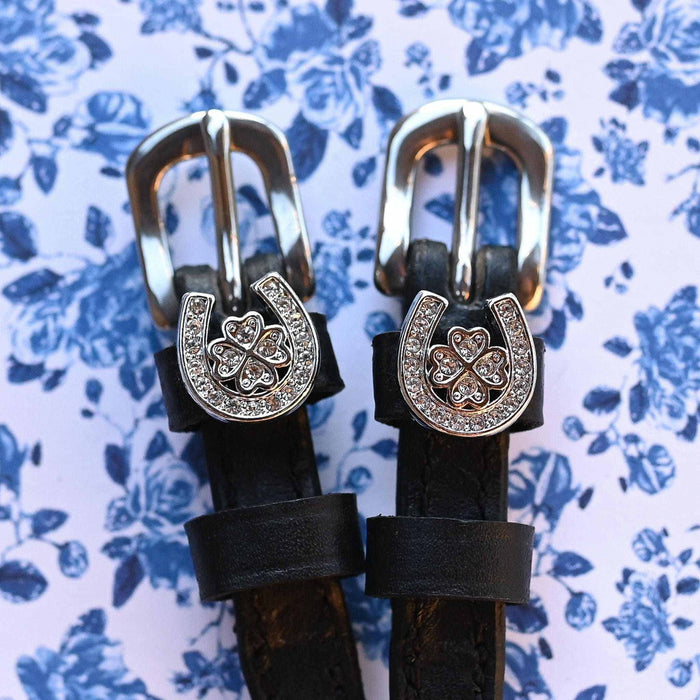 ManeJane spur straps with rhinestone horseshoe-clover charms on a blue floral background