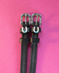 Black leather ManeJane spur straps with pastel horseshoe charms on a hot pink background