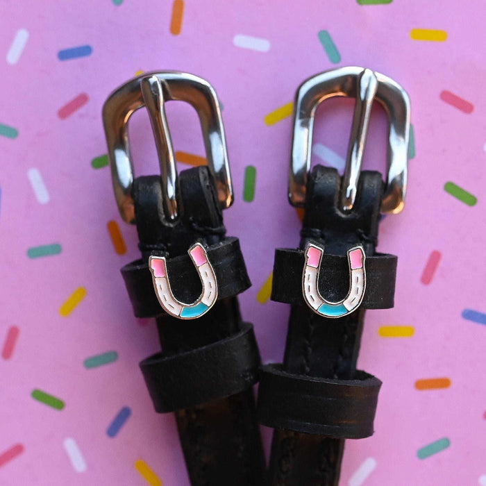 Silver buckles and horseshoe charms of spur straps on a pink confetti sprinkle background