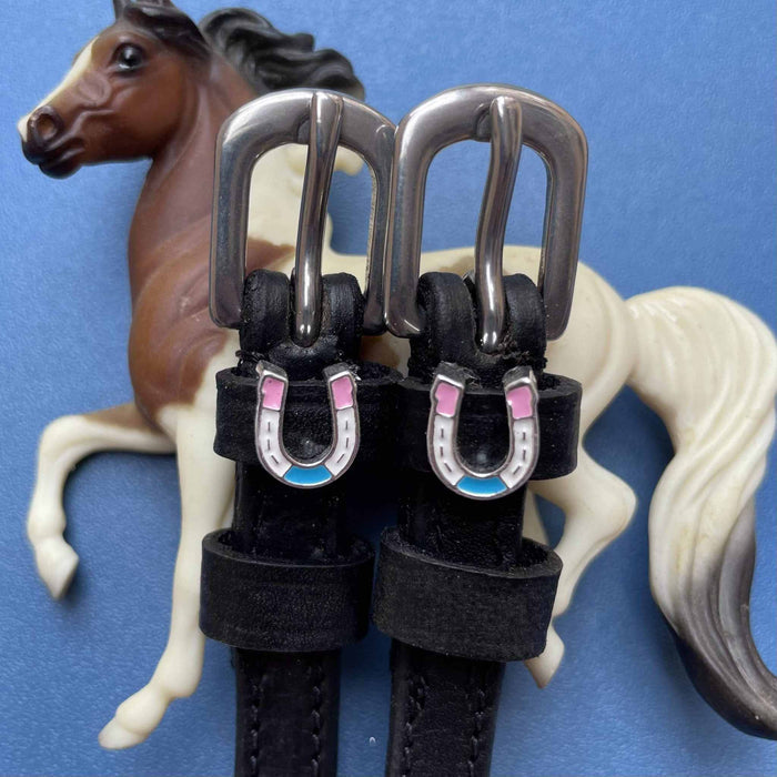 Pastel horseshoe charm spur straps styled with a toy horse figurine on blue