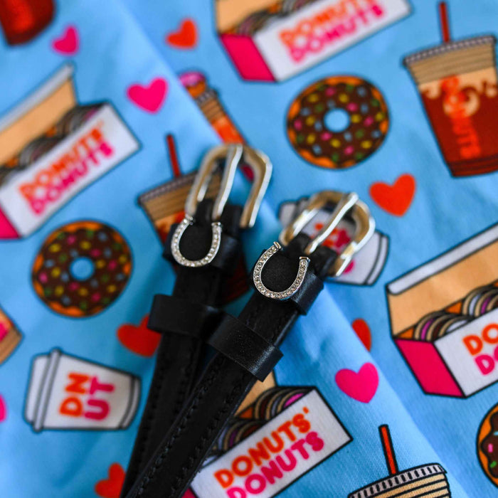 Silver horseshoe charm spur straps on a donut-print blue cloth, close-up of the buckles