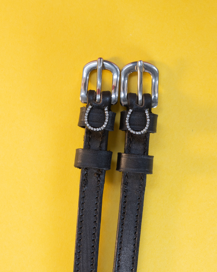 Pair of silver-bling horseshoe spur straps laid flat on a yellow background