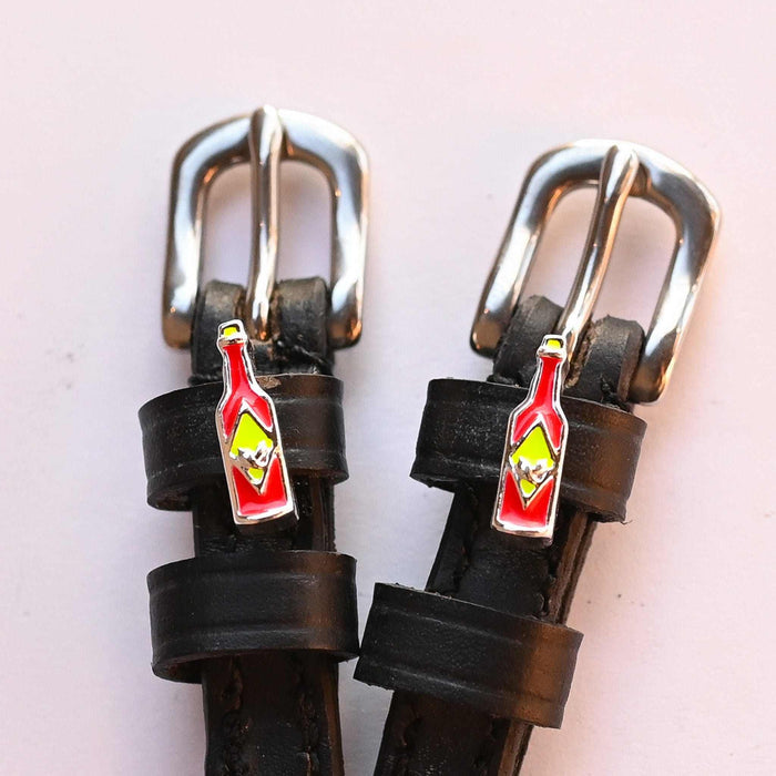 Close-up of hot sauce bottle charms and silver buckles on black spur straps