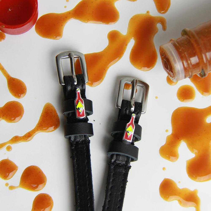 Hot sauce charm spur straps amid hot sauce splatters and a bottle on white