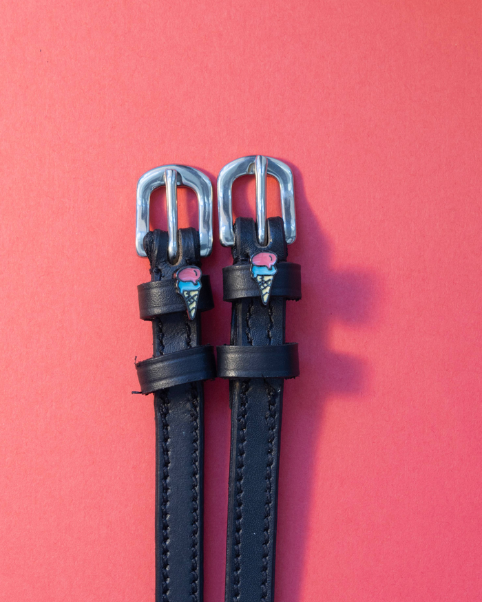 Black leather ManeJane spur straps with ice cream cone charms on a coral background
