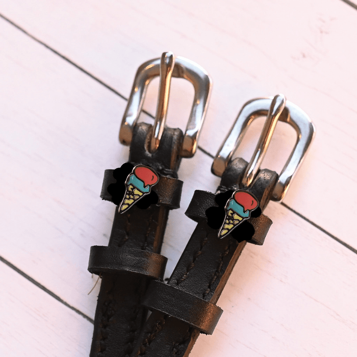 Silver buckles and ice cream cone charms of black leather spur straps on pink wood