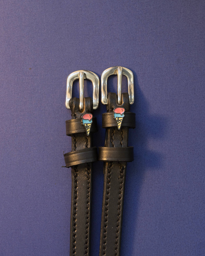 Ice cream cone spur straps in black leather with silver buckles on a periwinkle background