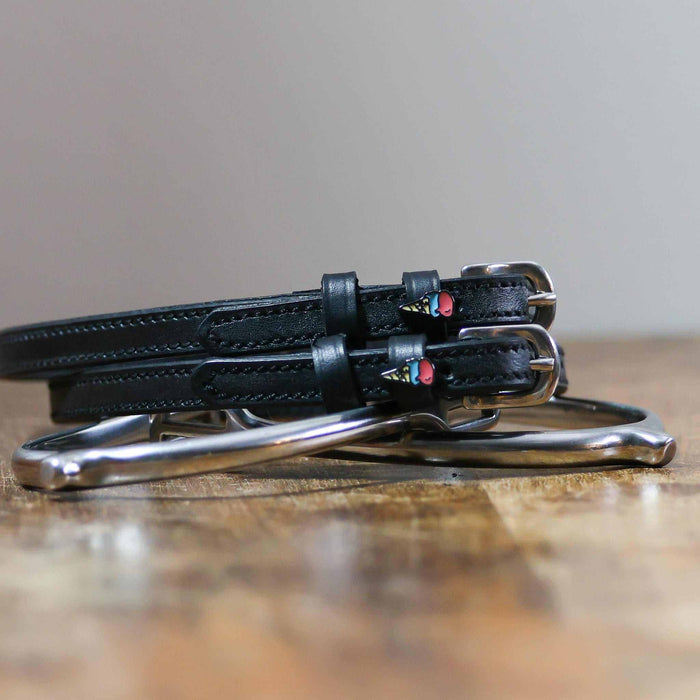 Black leather ice cream cone spur straps coiled beside a silver spur on wood