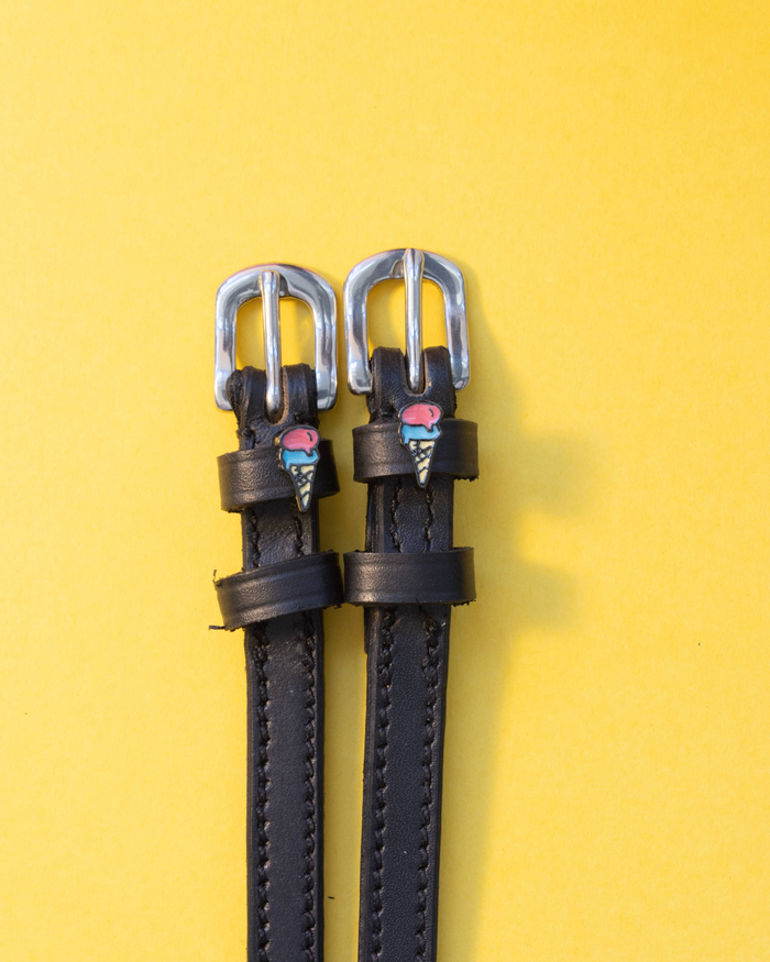 Pair of black leather ice cream cone spur straps with silver buckles on yellow