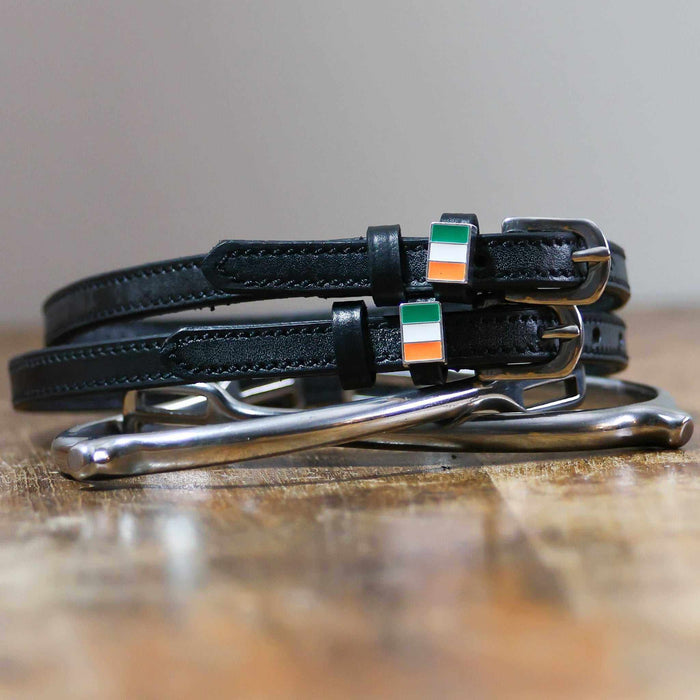 Black leather Ireland flag spur straps coiled beside a stirrup on wood