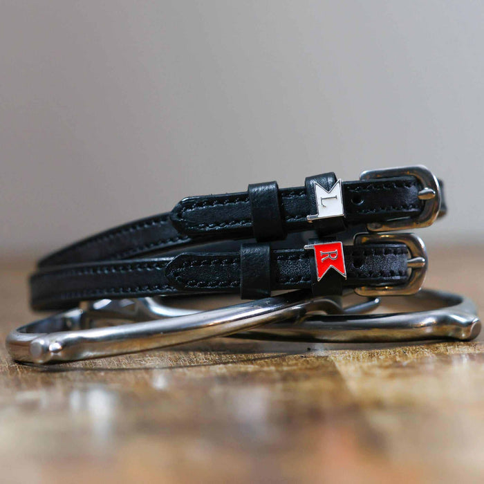 Black leather jump-flag spur straps coiled beside a silver stirrup on wood