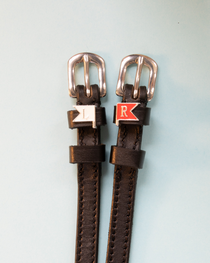 Brown leather ManeJane jump-flag spur straps with rose-gold buckles on pale blue