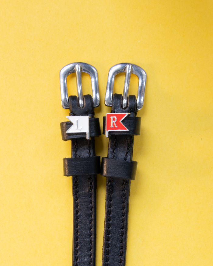 Black leather jump-flag spur straps with L and R charms on a yellow background