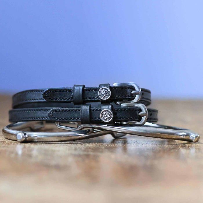 Black leather Leo zodiac spur straps coiled on wood beside a silver bit