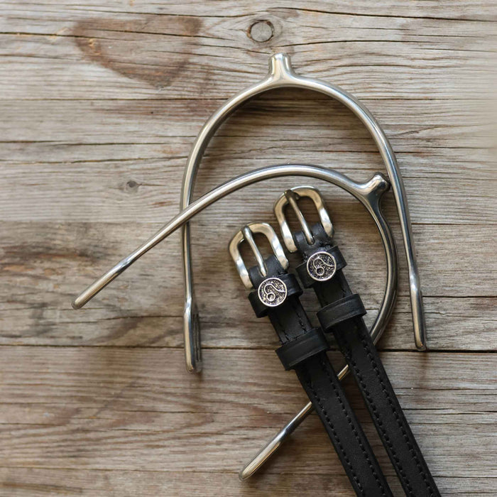 Black leather Leo spur straps arranged with a silver spur on weathered wood