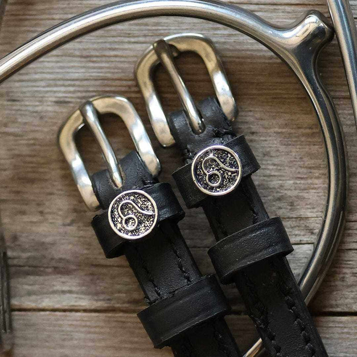 Close-up of Leo zodiac charm buckles on black leather spur straps beside a bit