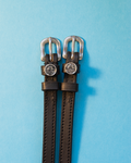Black leather ManeJane spur straps with round Libra zodiac charms on a bright blue backdrop