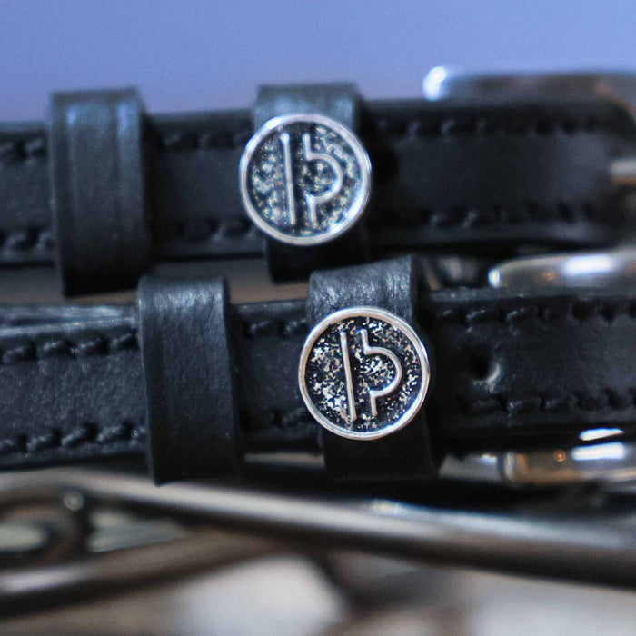 Close-up of silver Libra zodiac coin charms on black leather spur strap keepers