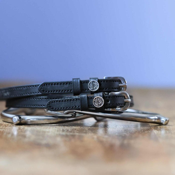 Black leather Libra zodiac spur straps coiled beside a silver spur on wood