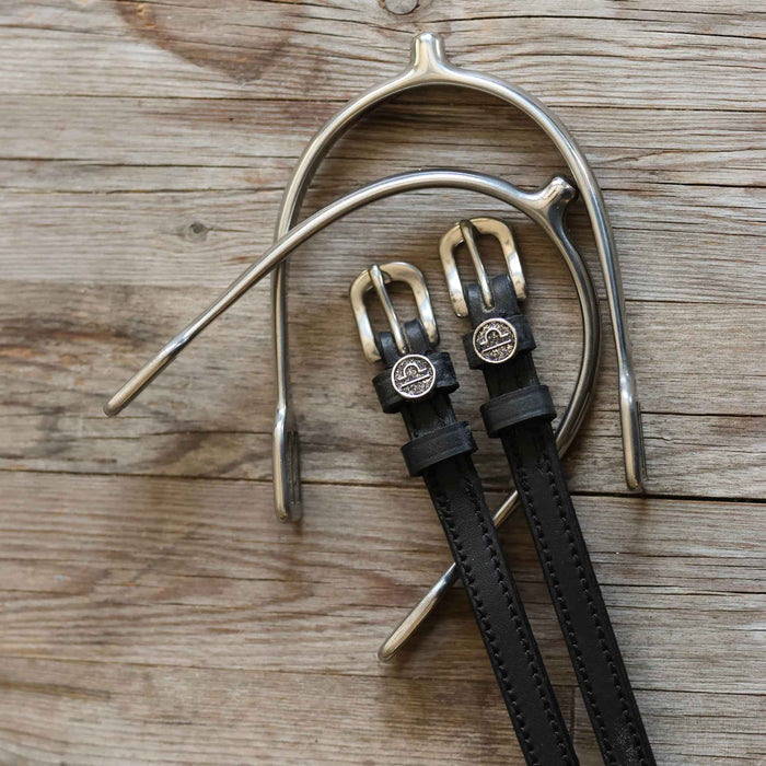 Black leather Libra spur straps arranged with a silver spur on rustic wood