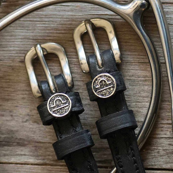 Close-up of round Libra zodiac medallion charms on black leather ManeJane spur straps