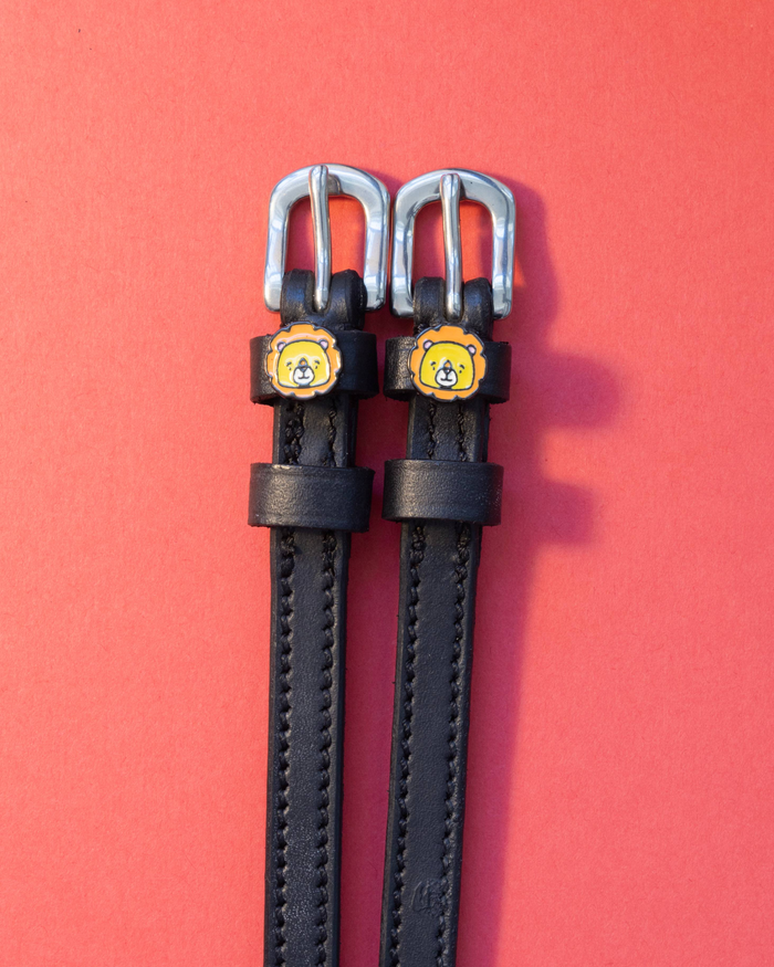 Black leather lion charm spur straps with silver buckles on a coral red background
