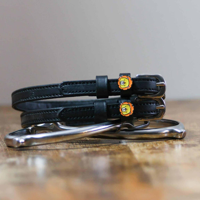 Black lion charm spur straps coiled beside a silver spur on a rustic wood surface