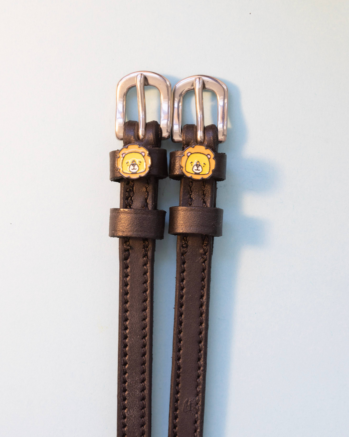 Dark brown leather lion charm spur straps with silver buckles on a pale grey background