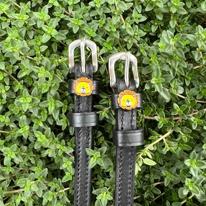 Black leather ManeJane lion spur straps set against green garden foliage