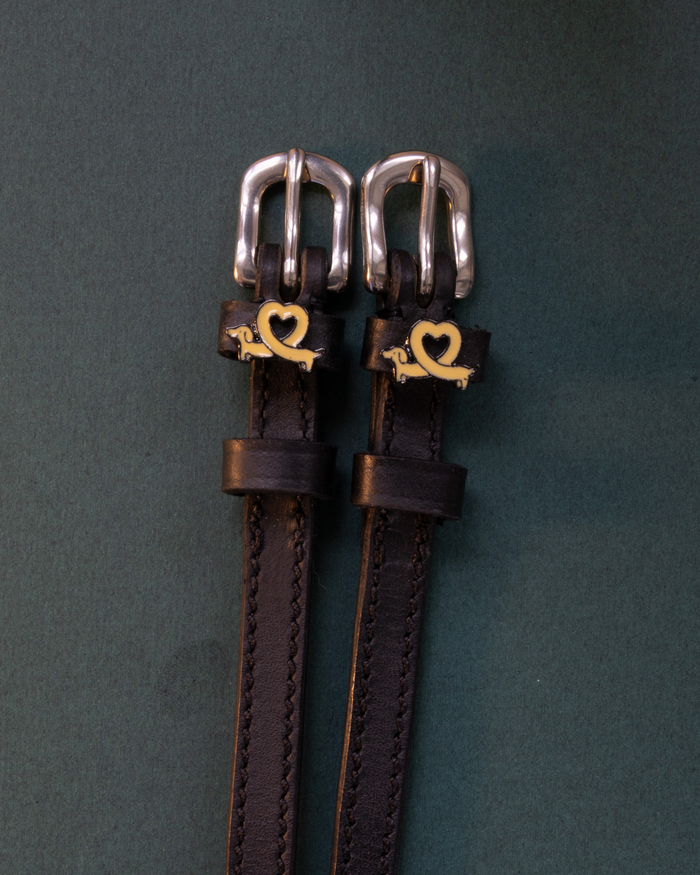 ManeJane Long Dogs spur straps with gold dachshund-heart charms on a dark green background