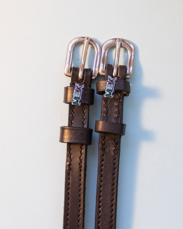 Brown leather ManeJane spur straps with metallic MEX charms and rose gold buckles on grey