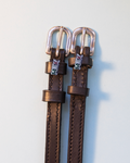 Brown leather ManeJane spur straps with metallic MEX charms and rose gold buckles on grey