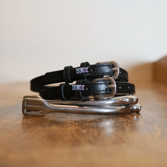 Black leather MEXico spur straps coiled beside a silver spur on a wooden surface